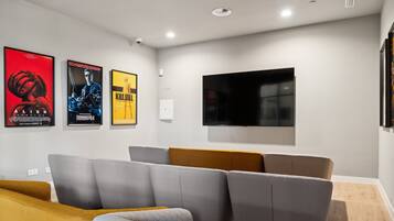 A modern cinema room with a large flat-screen TV, grey and mustard-colored seating, and three movie posters on the wall.