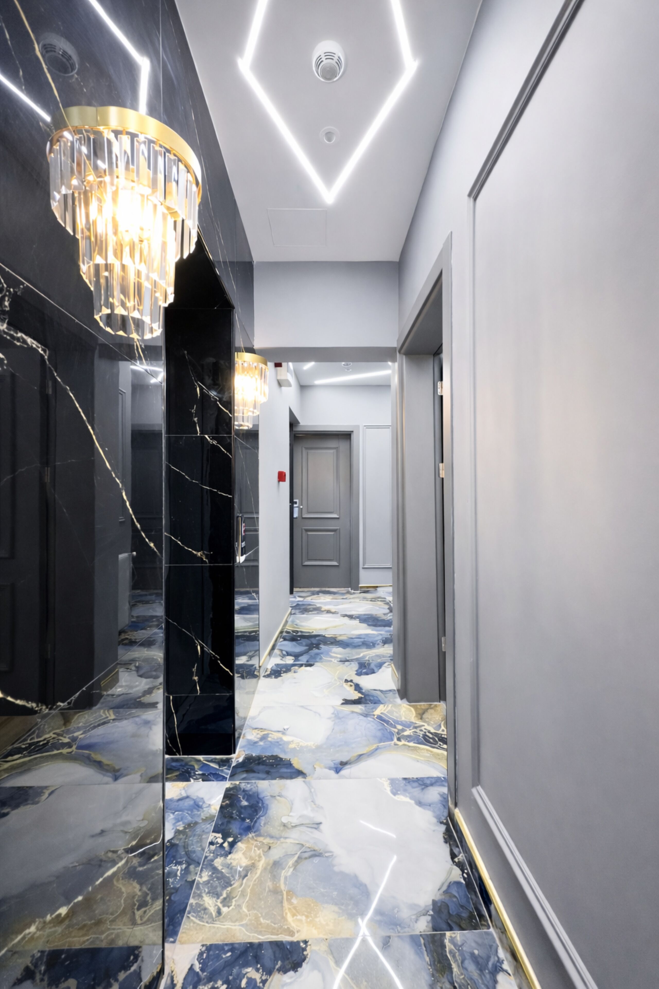 A hallway with a marble floor, a chandelier, and a door at the end.