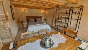 A cozy bedroom with a wooden bed, bedside tables, a nightstand, a shelf with baskets, and a table with a metal pitcher and candle. - Maison Spacieuse , Pour Séjours au Calme sur le Plateau des Mille Étangs (La Lanterne-et-les-Armonts)