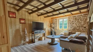 A cozy living room with a stone wall, wooden ceiling beams, a television, a sofa, and a small table. - Maison Spacieuse , Pour Séjours au Calme sur le Plateau des Mille Étangs (La Lanterne-et-les-Armonts)