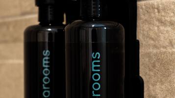 Deux flacons noirs de gel douche Gaiarooms, placés devant un mur à texture.