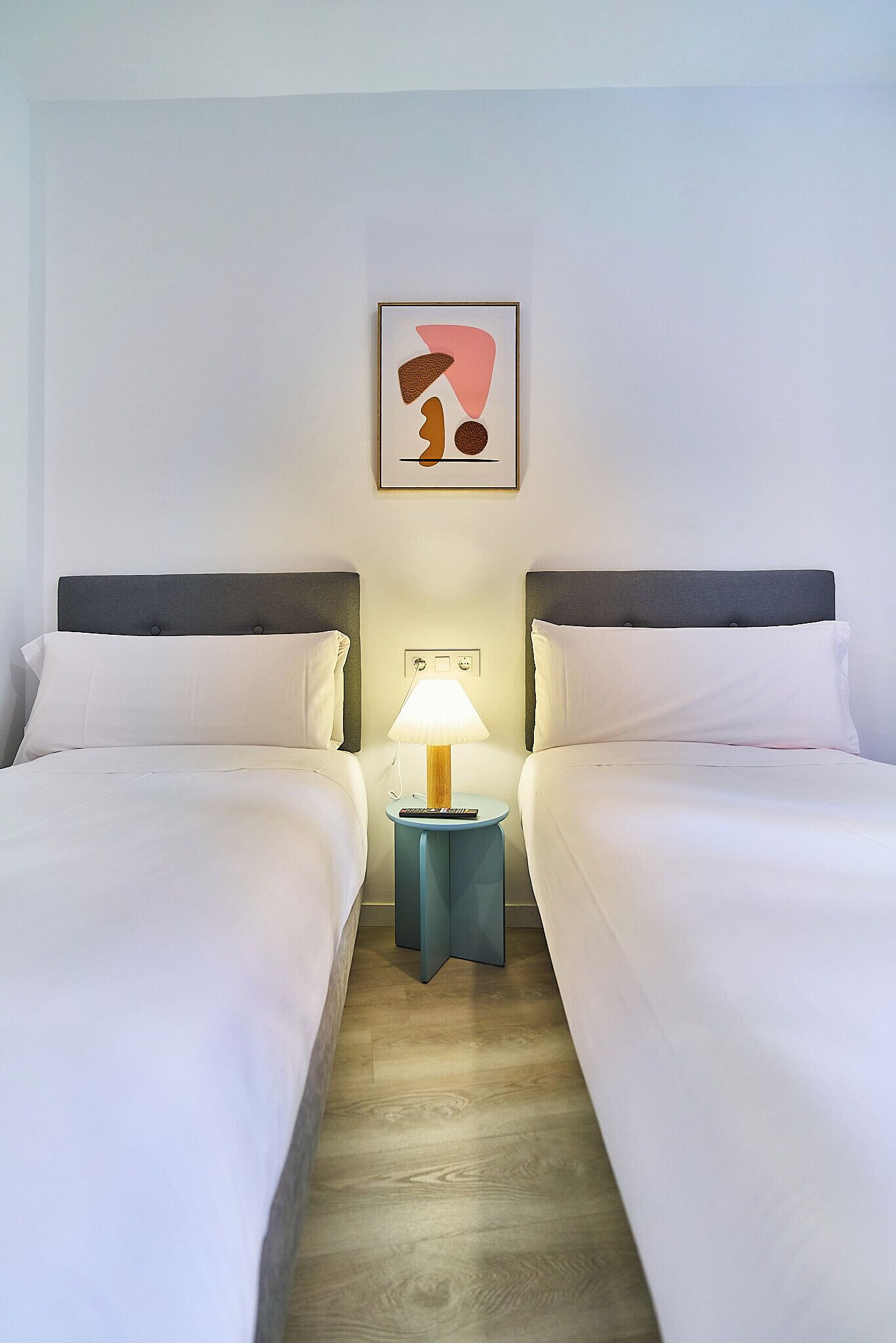A hotel room with two beds, a nightstand with a lamp, and a framed artwork on the wall.