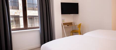 Habitación de hotel con cama, escritorio, silla, televisión y ventana con cortinas.