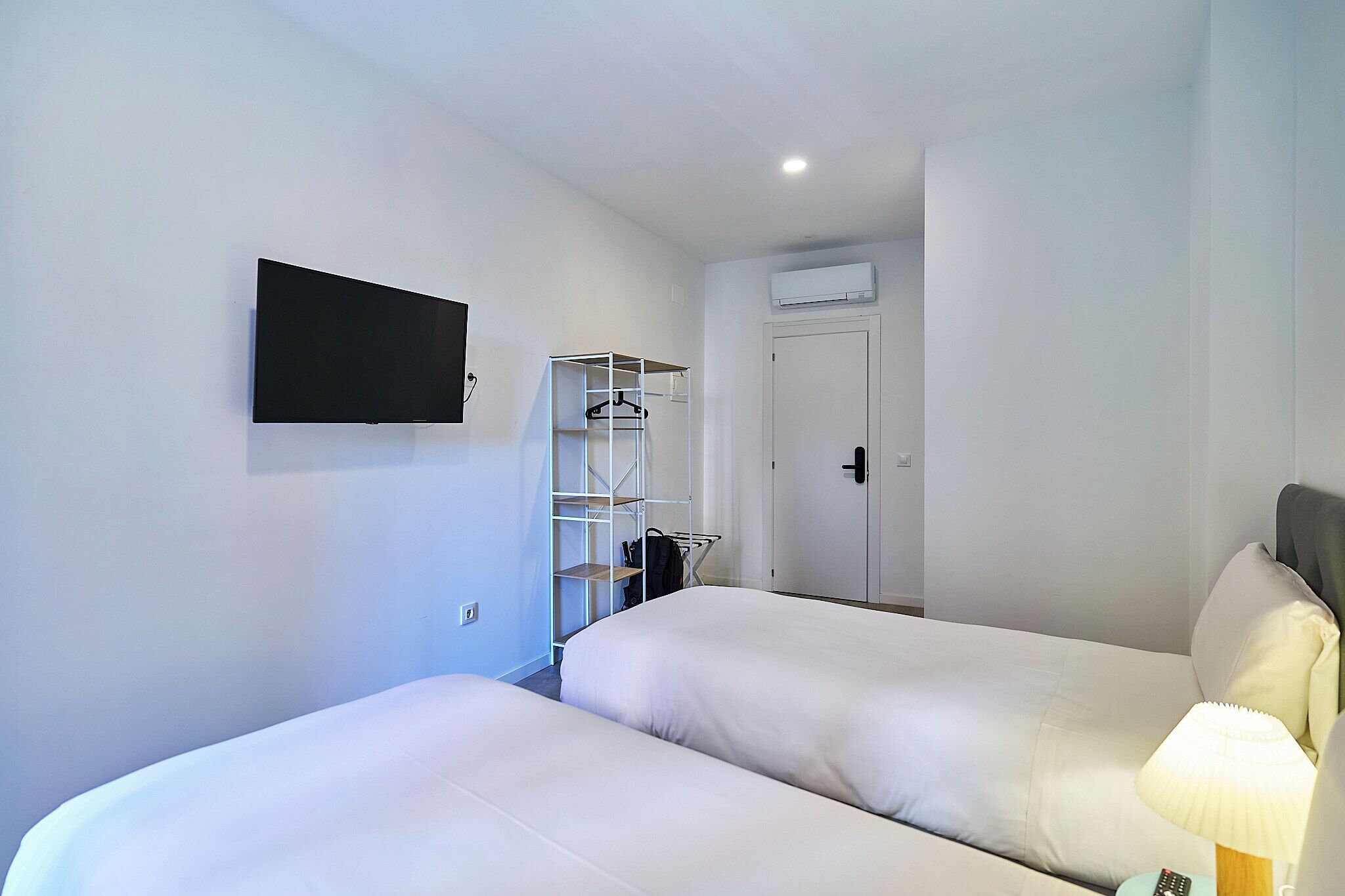 Habitación de hotel con dos camas, un televisor montado en la pared, un armario y un equipo de aire acondicionado.
