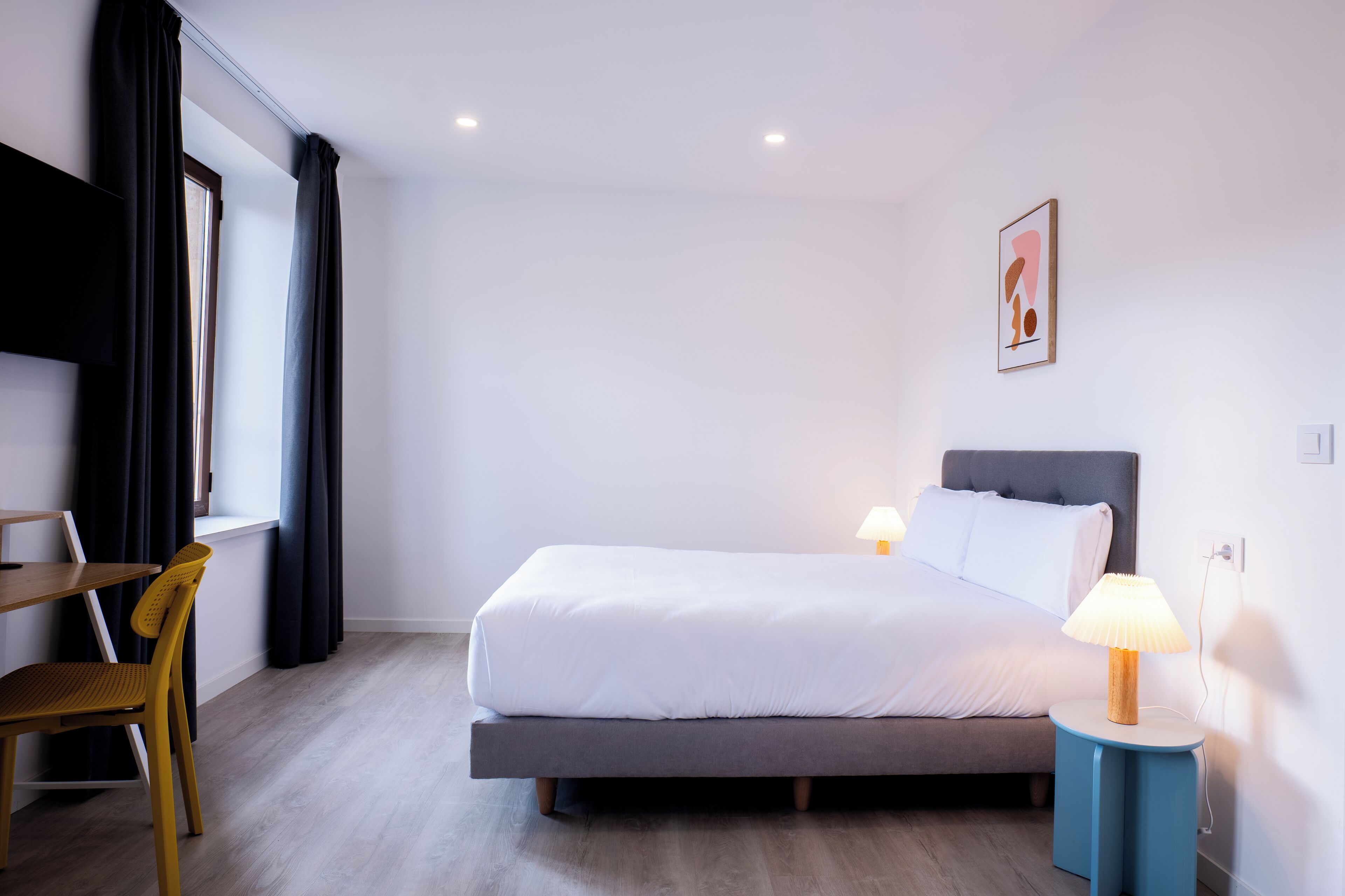 A modern hotel room with a bed, bedside table, lamp, and a chair.