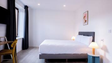 Una habitación de hotel moderna con una cama, mesita de noche, lámpara y una silla.