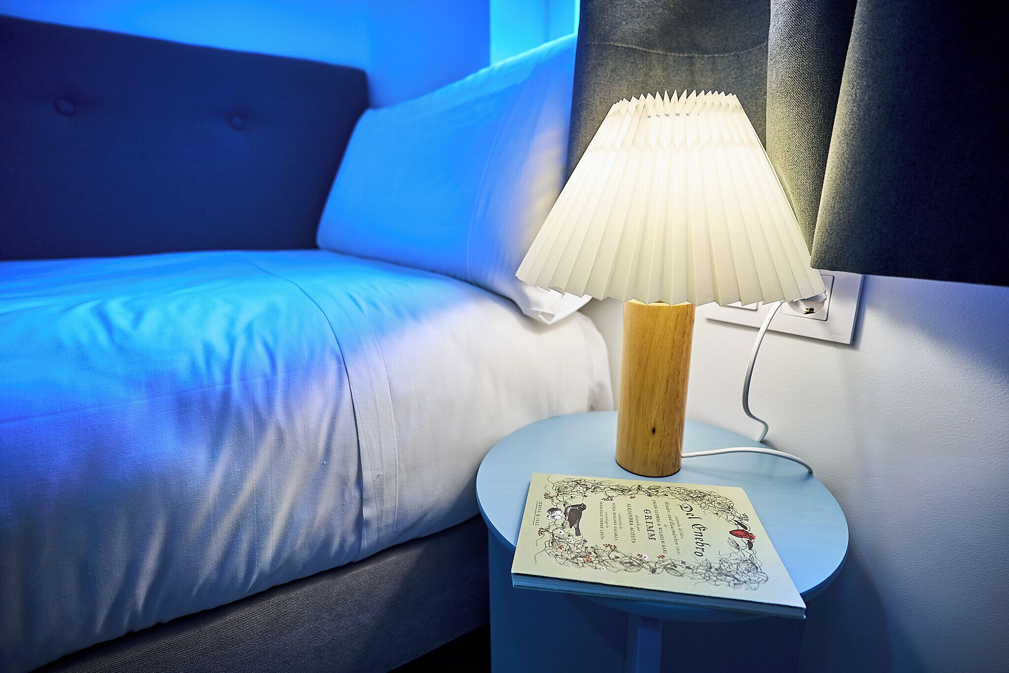 A bed with white bedding, a bedside table with a lamp, and a book.