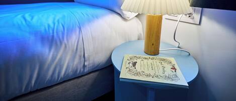 A bed with white bedding, a bedside table with a lamp, and a book.