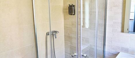 A modern bathroom with a glass-enclosed shower, a white toilet, and a sink with a towel hanging on the wall.