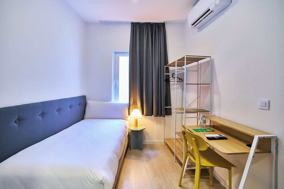 Una habitación de hotel con cama, escritorio, silla, lámpara y armario.
