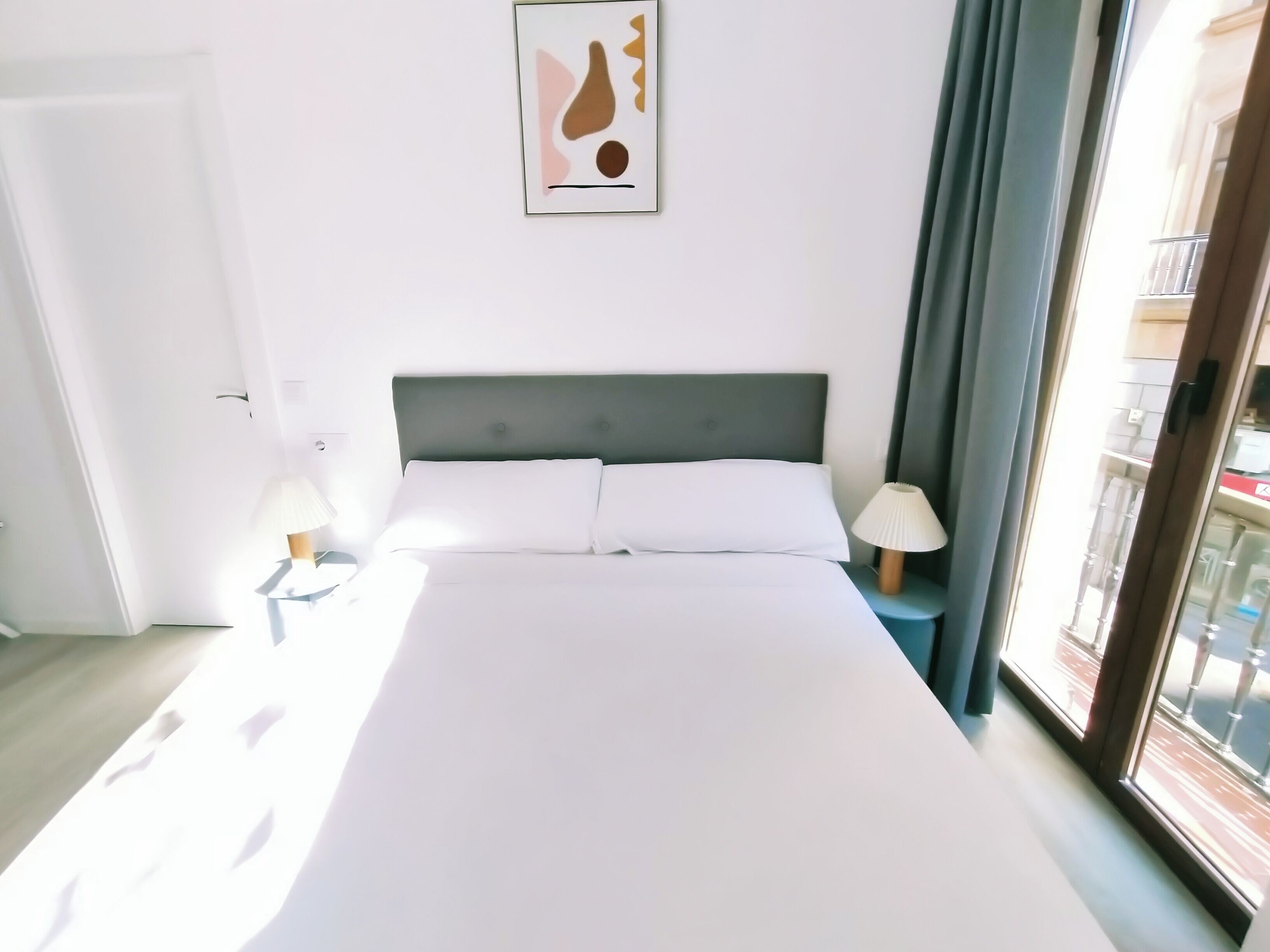 A hotel room with a large bed, two bedside lamps, a window with curtains, and a wall-mounted abstract painting.