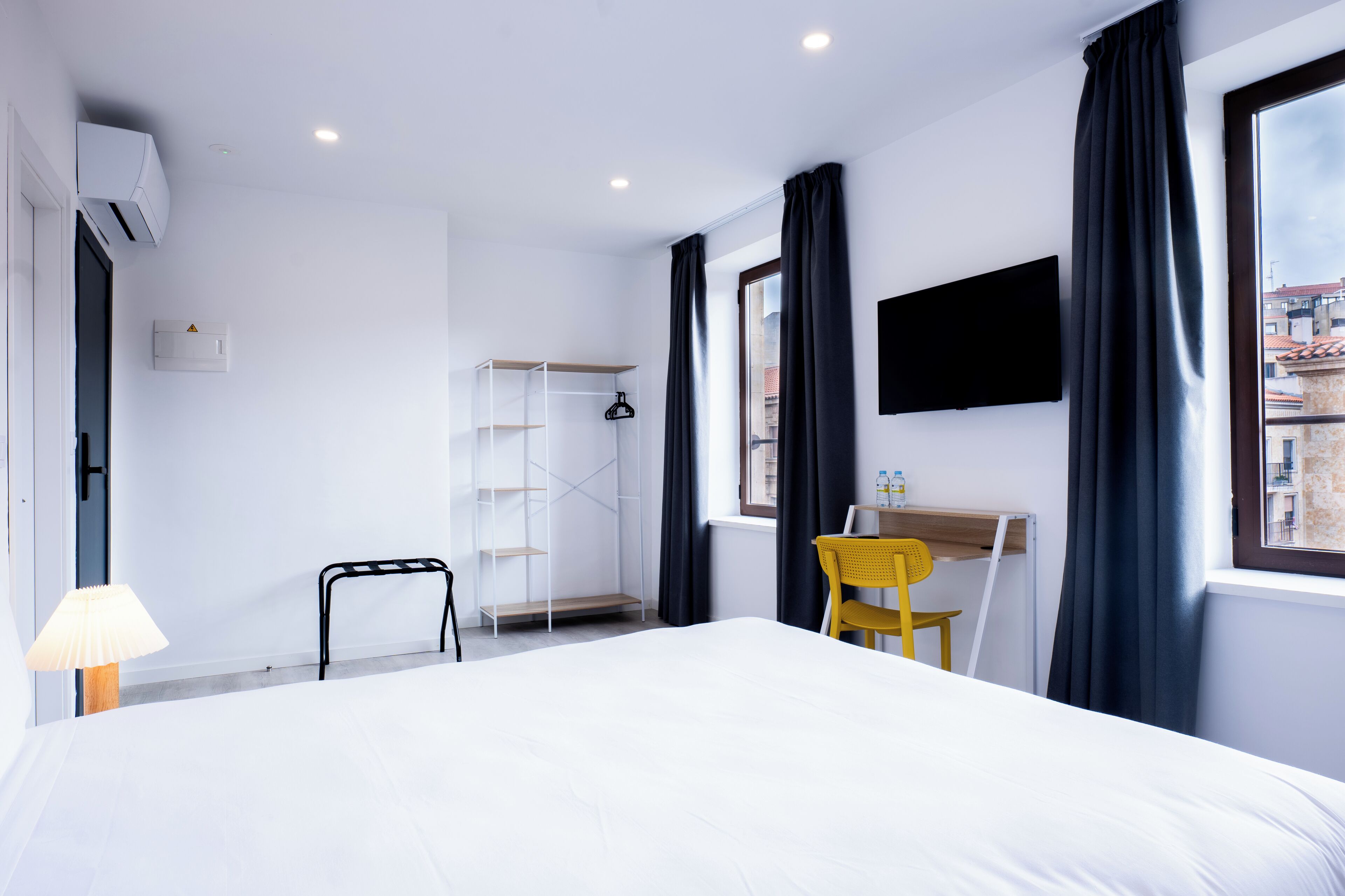Una habitación de hotel moderna con una cama grande, un escritorio con silla, un televisor montado en la pared y una ventana con cortinas.