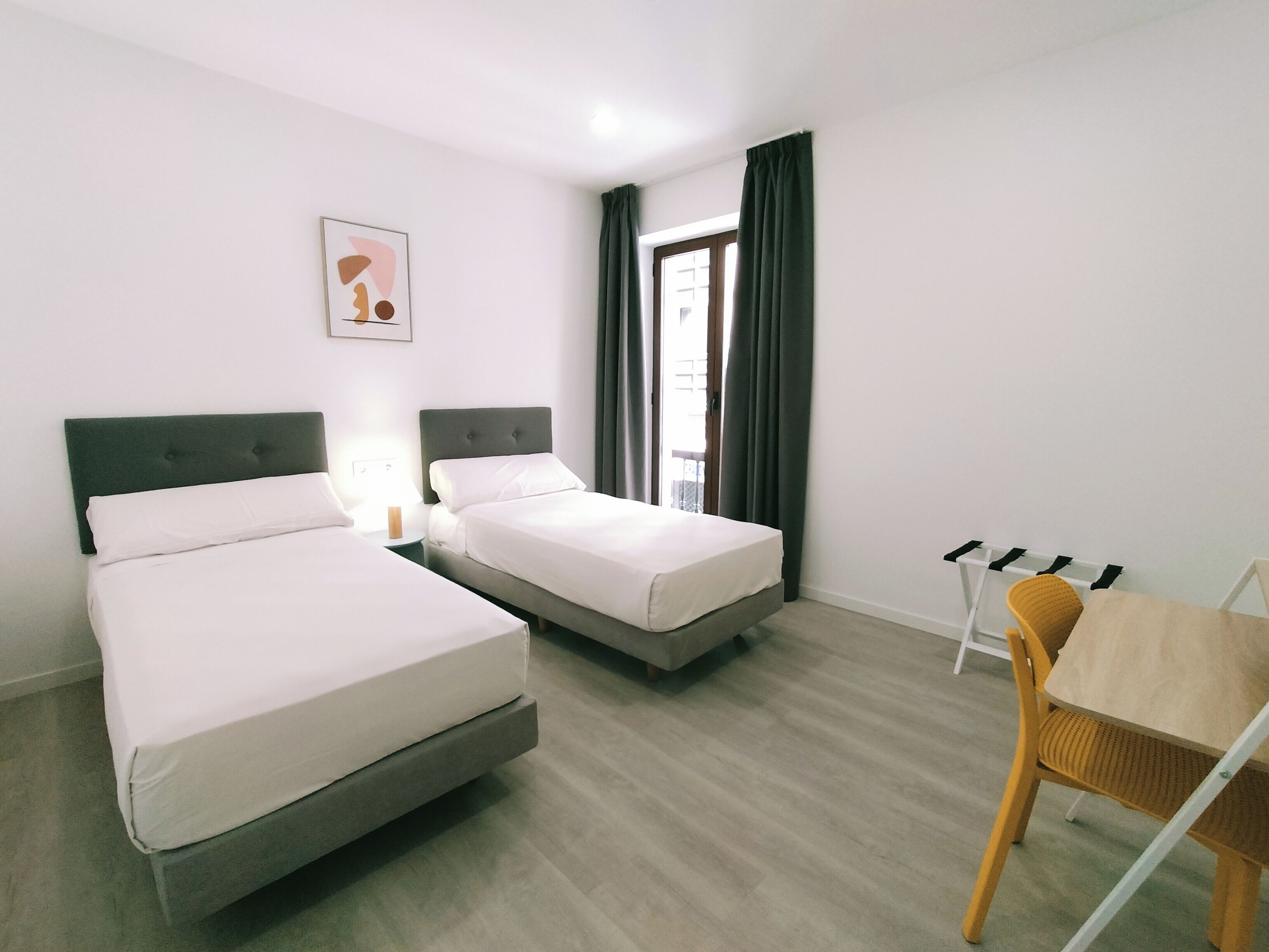 Habitación de hotel con dos camas, una mesita pequeña y una silla.