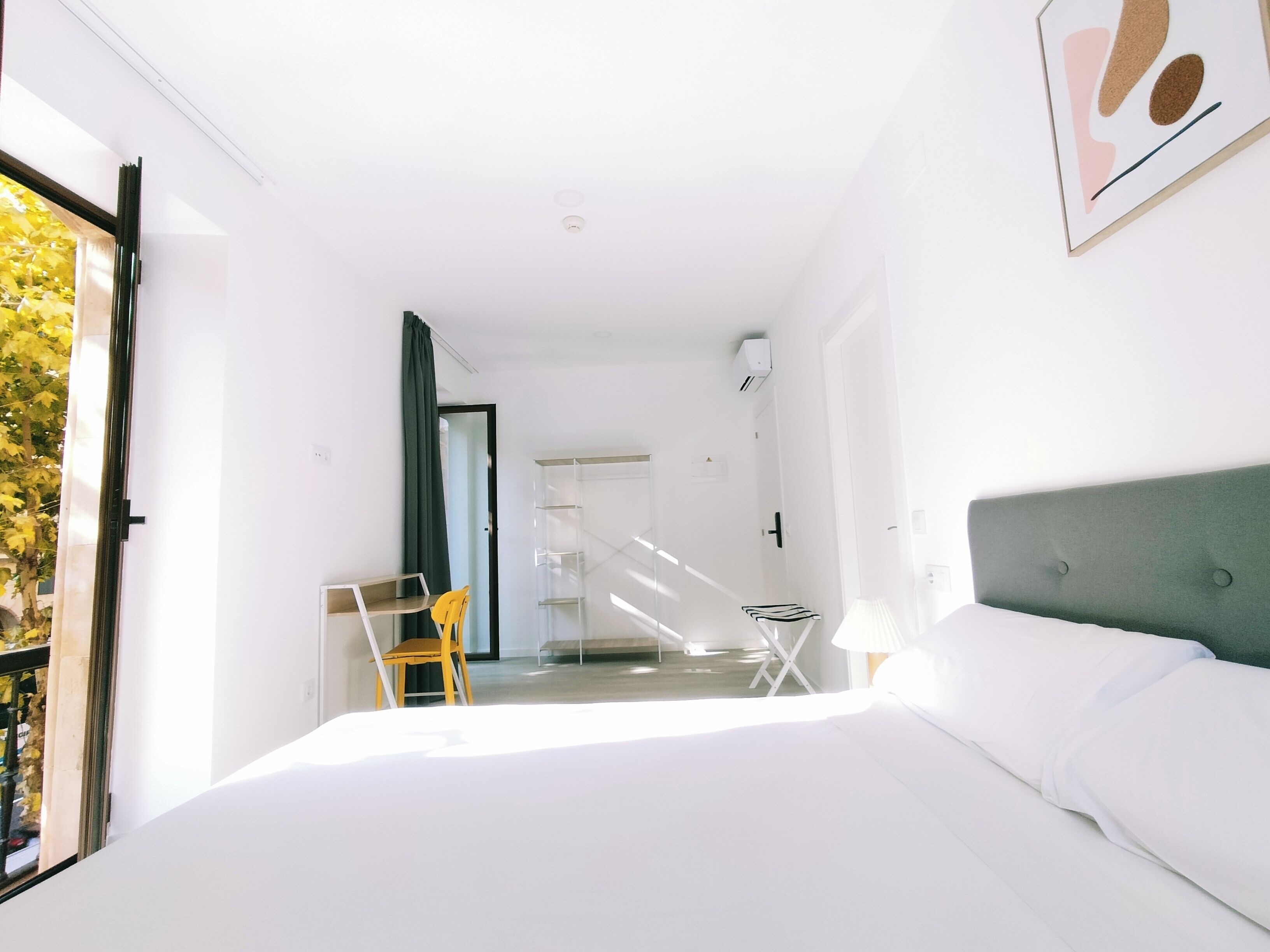 A modern hotel room with a large bed, a desk, a chair, and a view of the outdoors.