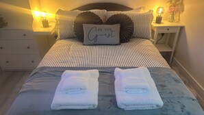 A neatly made bed with striped bedding, a pillow with the text "BE OUR Guest," and two folded towels on the bed.