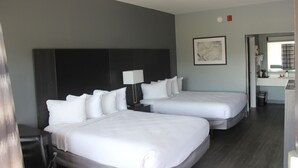 A hotel room with two beds, a dark headboard, a bedside table with a lamp, and a framed picture on the wall.