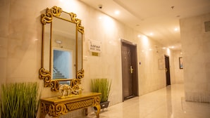 A hallway with a large ornate mirror, a gold console table, and potted plants.