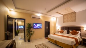 A hotel room with a large bed, a TV mounted on the wall, a potted plant, and a desk with a chair.