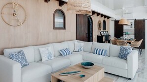 Una sala moderna con un sofá seccional grande, una pared de acento de madera, un reloj redondo y una zona de comedor con muebles de mimbre.