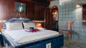 Habitación de hotel con una cama grande, paneles de madera, pared de azulejos y una pequeña mesa con una silla.