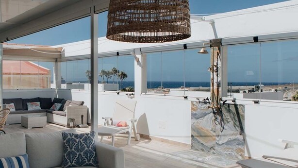 Una terraza moderna en la azotea con un sofá, sillas y una lámpara colgante.
