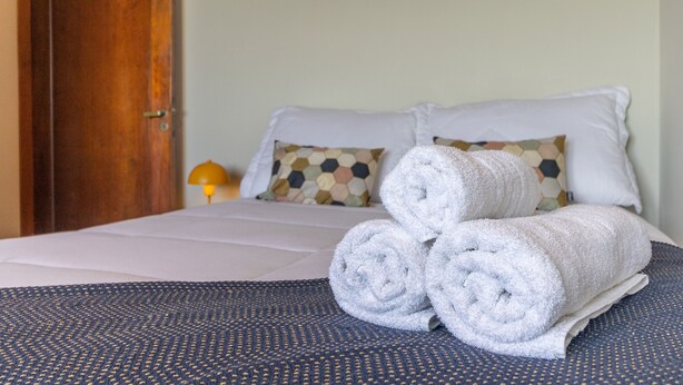 A neatly made bed with rolled towels, a patterned bedspread, and a hexagonal-patterned pillow. - Apartamento Amplo Prox HC São Paulo (São Paulo)