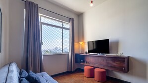 A modern living room with a sofa, a TV on a wooden console, and a large window with curtains. - Apartamento Amplo Prox HC São Paulo (São Paulo)