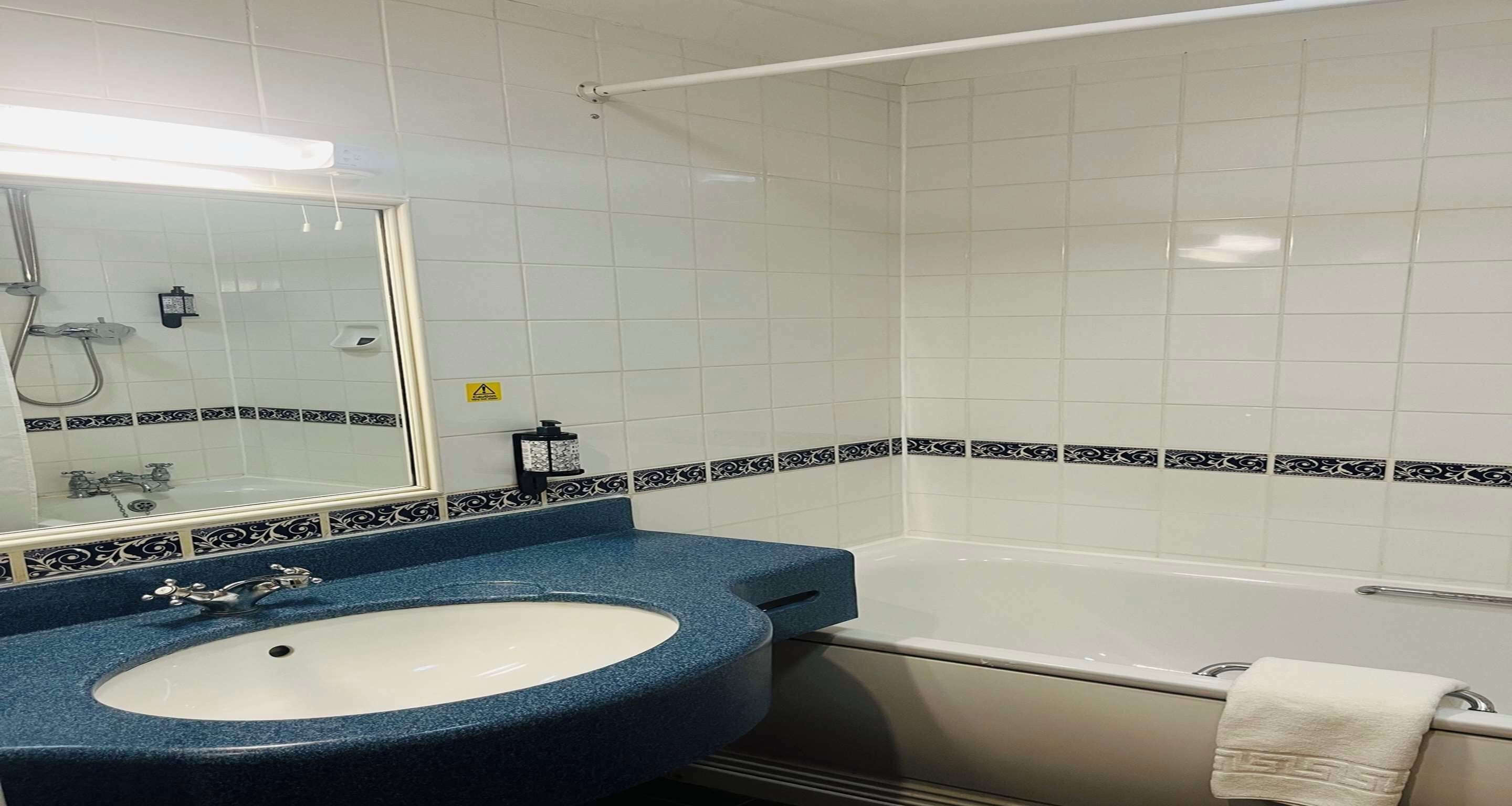 A bathroom with a white bathtub, a sink with a blue countertop, and a mirror.