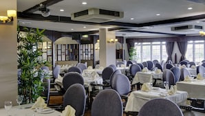 Un restaurante con varias mesas dispuestas para comer, con una decoración clásica que incluye candelabros y ventanas amplias.