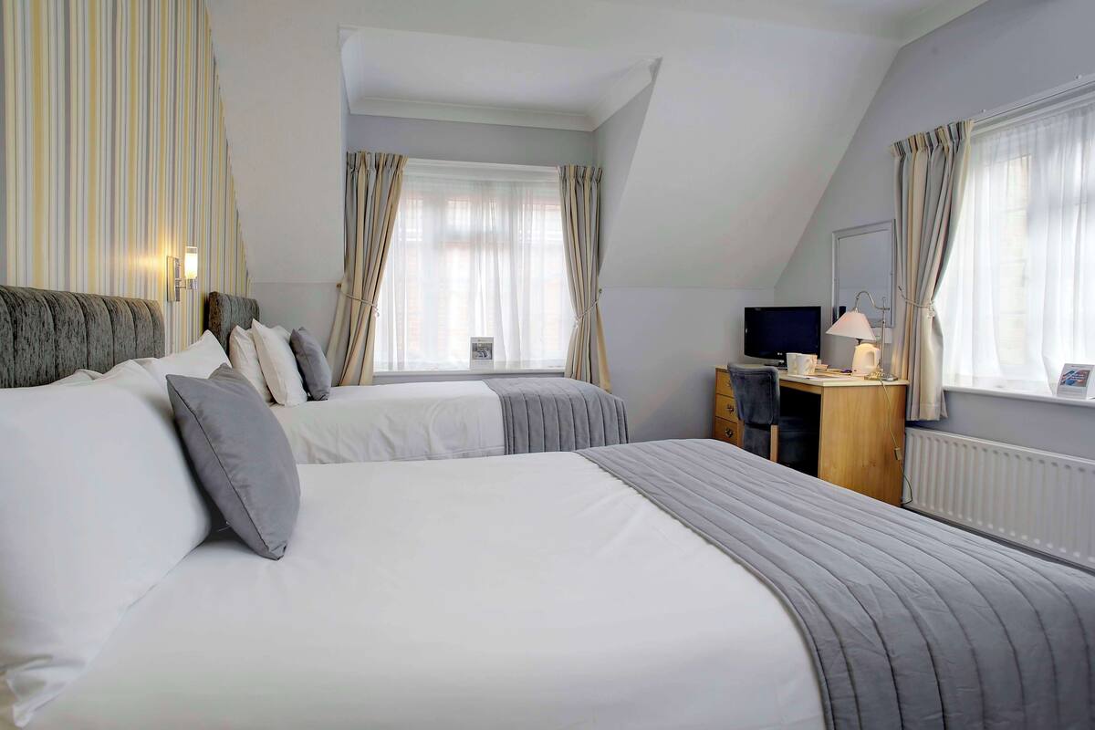 Une chambre avec deux lits, un bureau, une télévision et une fenêtre avec des rideaux.