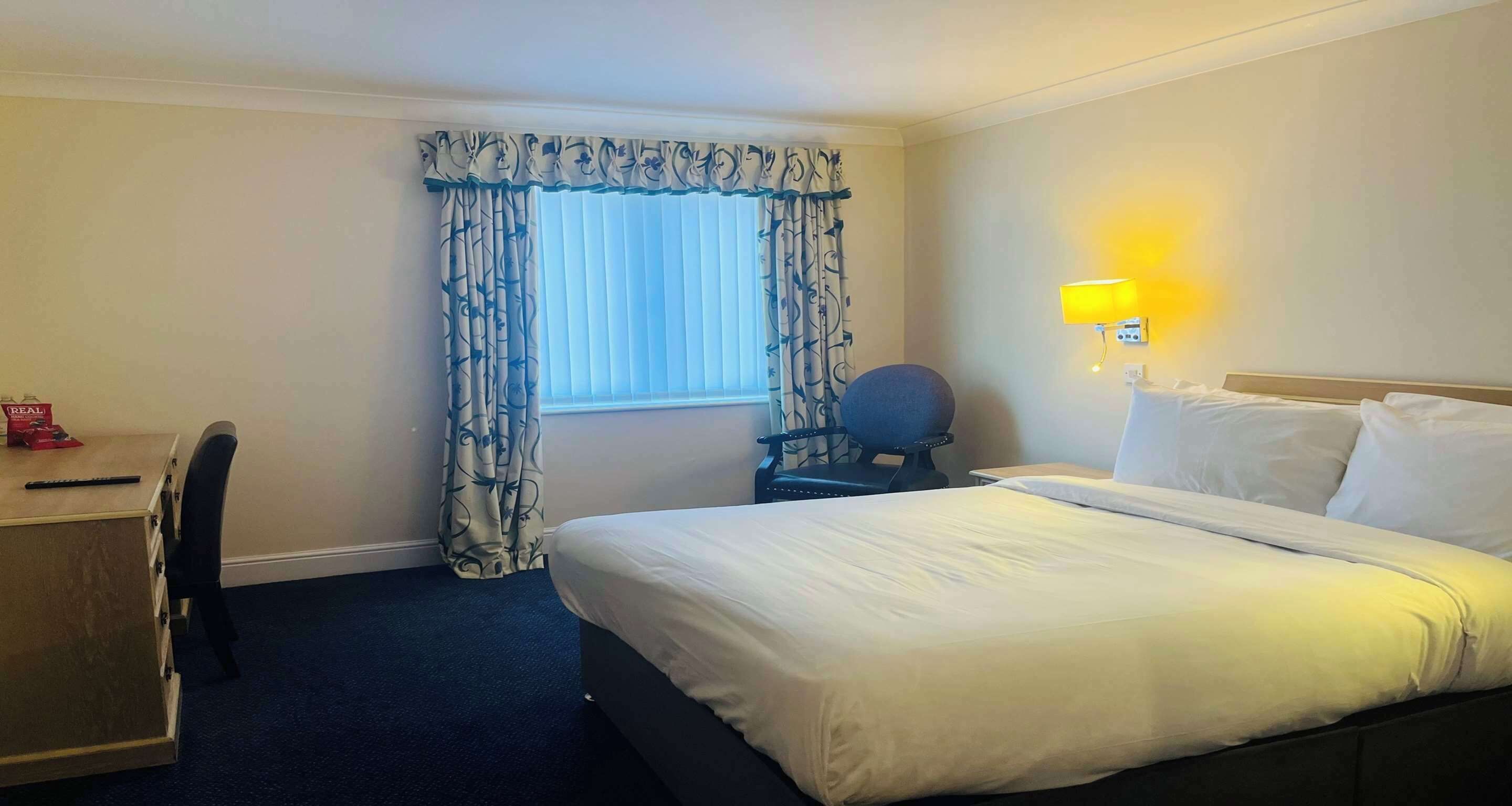 A hotel room with a bed, a desk, a chair, and a window with curtains.