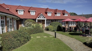 Un edificio de techo rojo, paredes de ladrillo y un camino pavimentado que conduce a una zona de estar exterior con sombrillas.