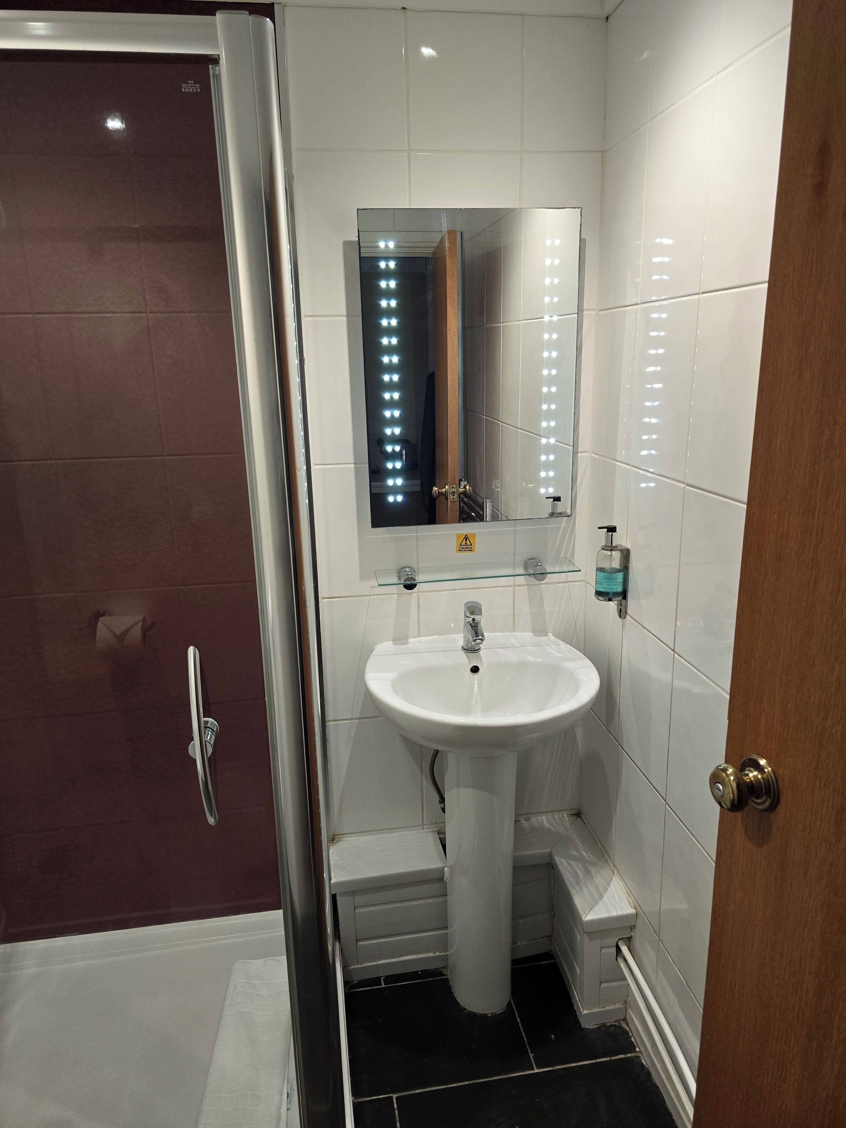 Un baño con lavamanos blanco, espejo y zona de ducha.