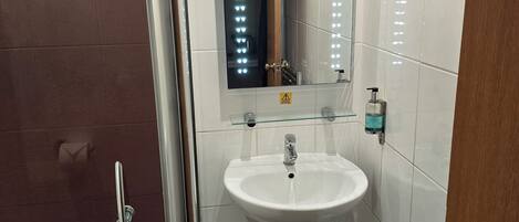 Un baño con lavamanos blanco, espejo y zona de ducha.