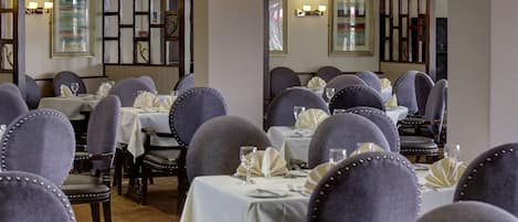 Un restaurante con varias mesas y sillas, cada conjunto con manteles y servilletas blancos.