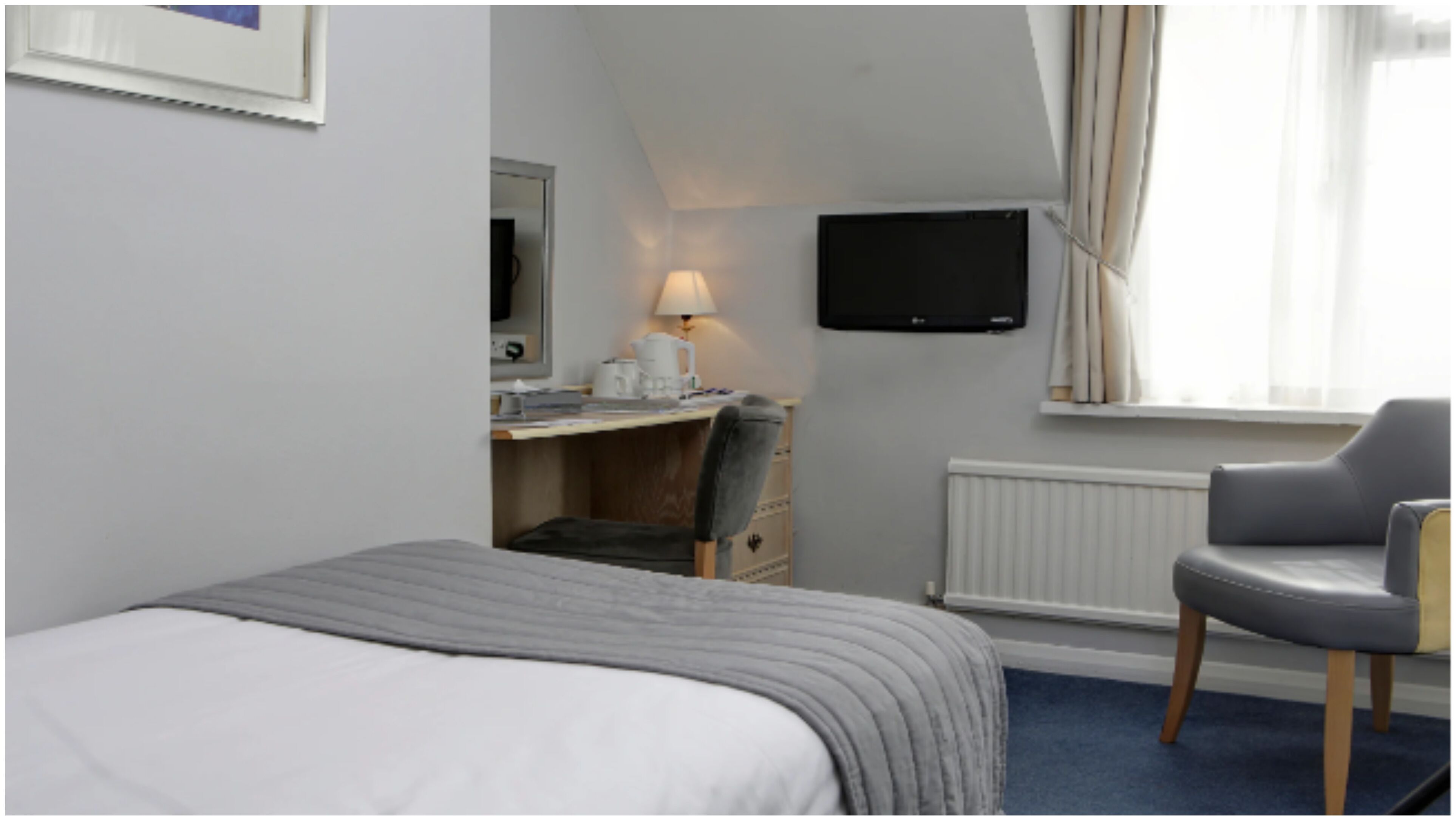 A hotel room with a bed, a desk with a chair, a television, and a window with curtains.