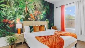 A bedroom with a large bed, a nightstand, a lamp, a potted plant, and a tropical mural on the wall. - Beautiful, Cozy, Contemporary 4BR near Downtown Dallas
 (Dallas)