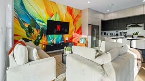 A modern living room with a large TV, comfortable seating, and a vibrant abstract wall mural. - Beautiful, Cozy, Contemporary 4BR near Downtown Dallas
 (Dallas)