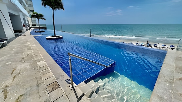 A swimming pool with clear blue water, a palm tree, and a view of the ocean.