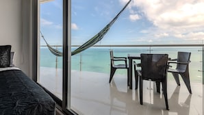 A balcony with a view of the ocean, a hammock, and a table with chairs.