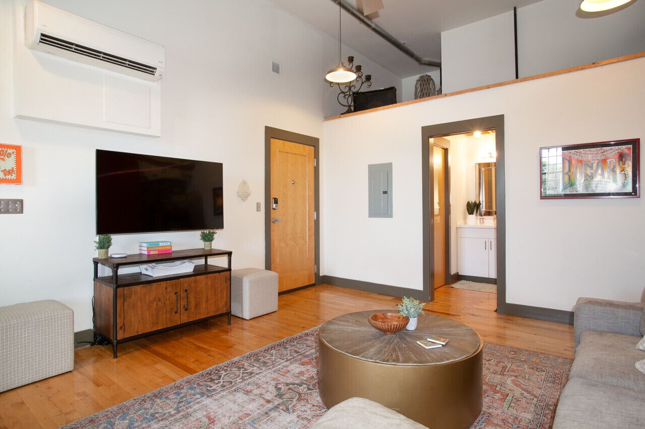 Uma sala de estar moderna com televisão de tela plana, piso de madeira, uma mesa de centro redonda e um sofá.