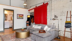 A modern living room with a grey sectional sofa, a round gold coffee table, and a red curtain.