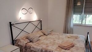 Una cama bien tendida con un edredón estampado, una mesita de noche y una lámpara de pared con la palabra 'love'.
