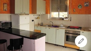 Una cocina con armarios blancos, estufa a gas, horno y ventana con persianas.