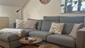 Ett modernt vardagsrum med en grå soffa, två runda soffbord och en träklocka på väggen.