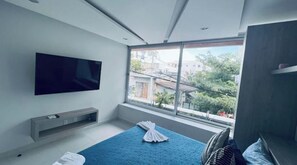 Relax in a spacious room with a large flat-screen TV, a comfortable bed, and a window offering a view of the surrounding landscape.