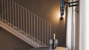 A modern dining area with a round table, two chairs, a bottle of champagne, and two glasses. A staircase with a railing is visible in the background. - Valèt guesthouse, four rooms and sleeps 12, half an hour from Alba (Moasca)