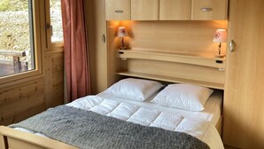 Ein hölzernes Etagenbett mit zwei Kissen und einer Decke, ein Fenster mit Blick auf Grün und ein pinkfarbener Vorhang.