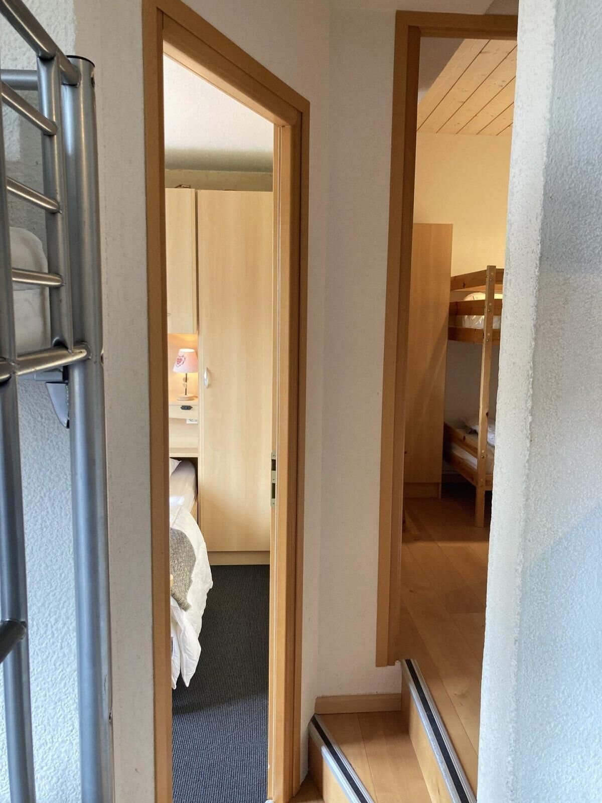 Un couloir étroit avec une porte en bois donnant sur une chambre où se trouve un lit superposé.