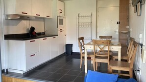 Eine kompakte Küche mit weißen Schränken, einer schwarzen Arbeitsplatte und einem Essbereich mit Holztischen und einem Tisch.